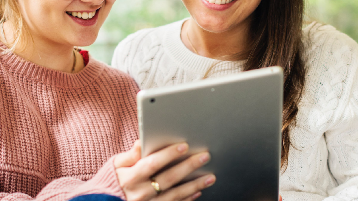 Two women smiling over a shared tablet.