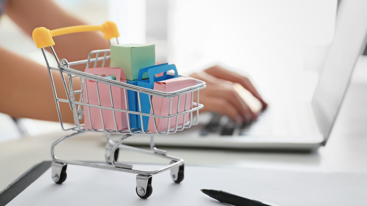 Minature shopping cart sits in front of woman working her online retail business.