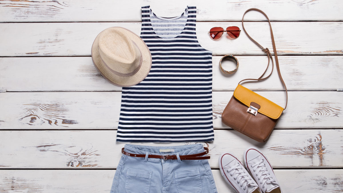 Striped shirt, straw hat, leather purse and other accessories on a flat lay.
