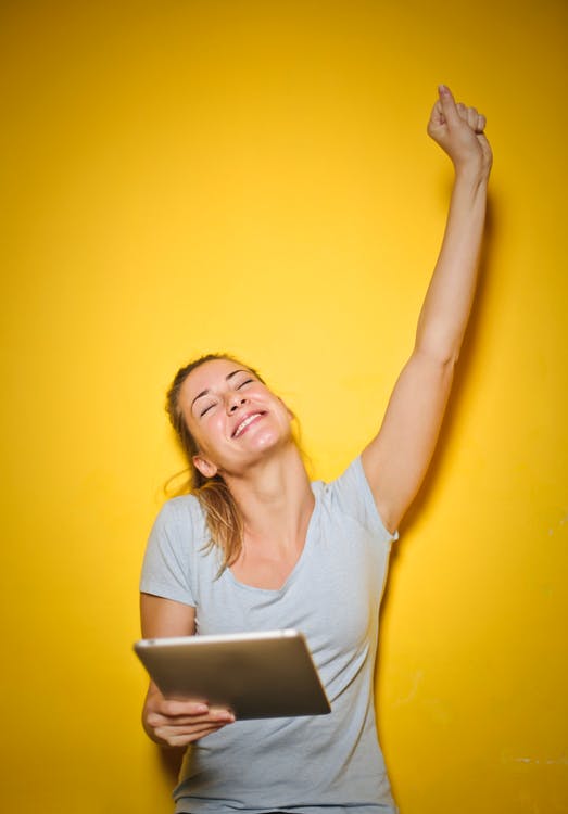 Woman smiling and raising her hand while holding a tablet