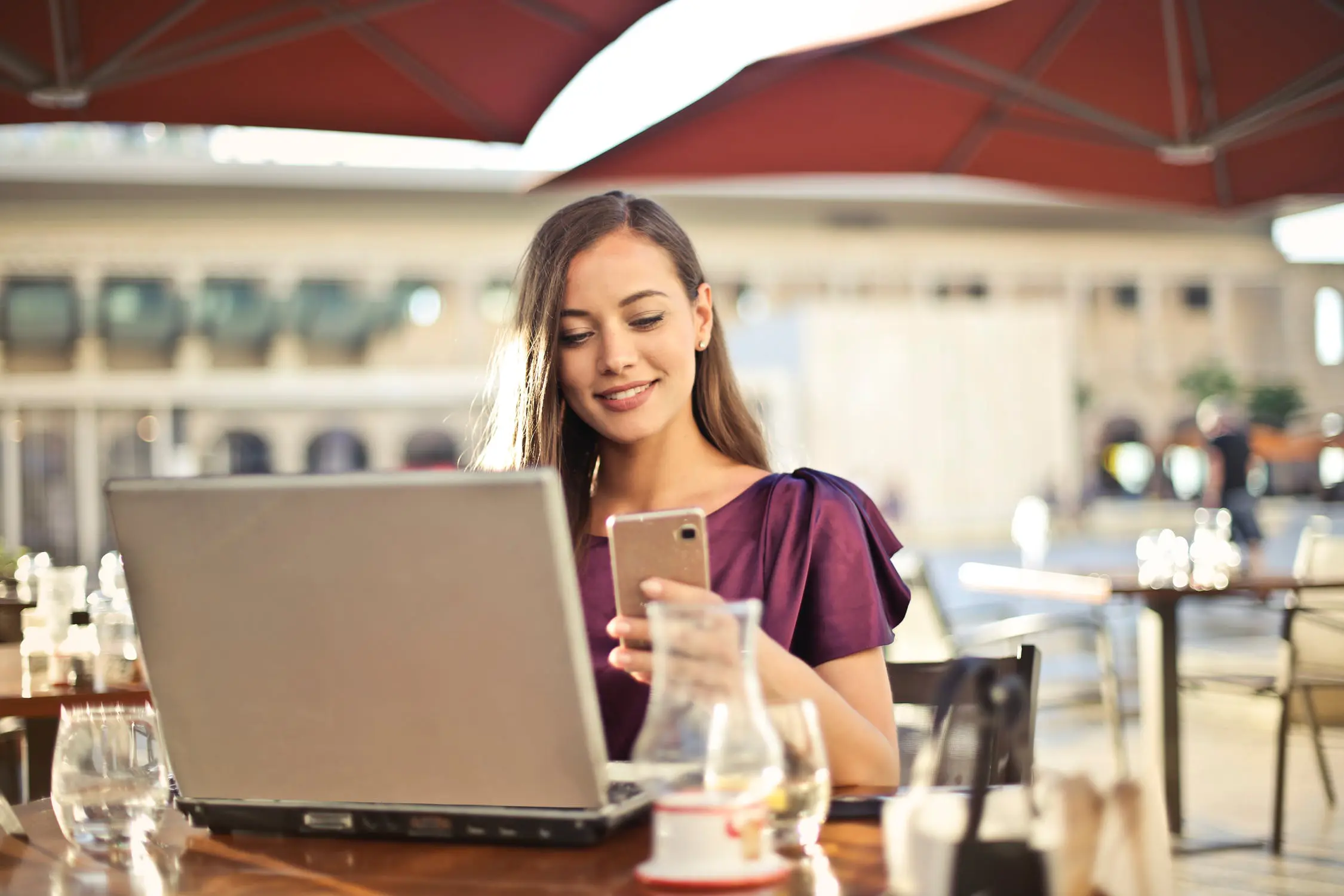 Smiling woman looks at phone while on her laptop